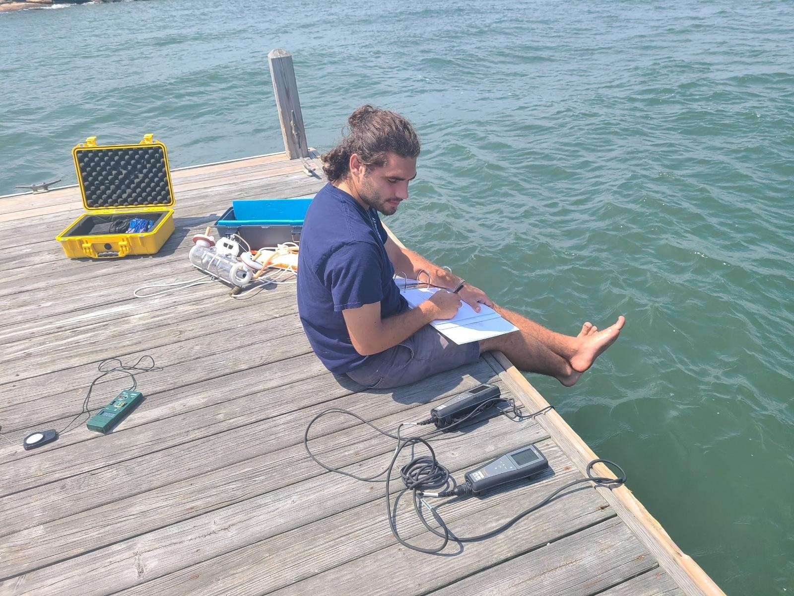 Man sitting on pier writing test results in notebook from testing water quality
